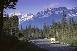 Camper travelling down Alaskan road with mountain view.
